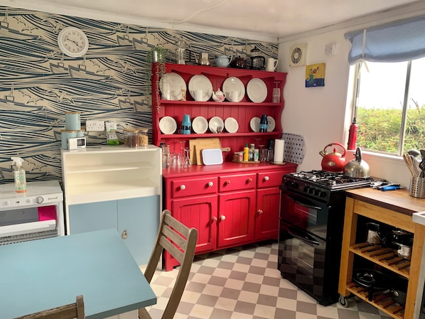 Una cocina con un armario rojo, una estufa y una ventana con vistas a zonas verdes.