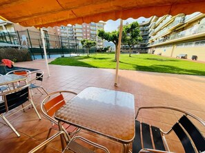 Un espace extérieur aménagé en terrasse avec une table et des chaises, un court de tennis en arrière-plan et une pelouse verdoyante.