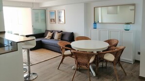 A modern living room with a grey sofa, wicker chairs, a white round table, and a large mirror on the wall. - RECONNECTAR Malgrat de Mar Garbí I (Malgrat de Mar)