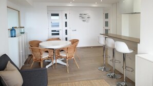 A modern kitchen with white cabinets, a round dining table with wicker chairs, and a bar area with white stools. - RECONNECTAR Malgrat de Mar Garbí I (Malgrat de Mar)