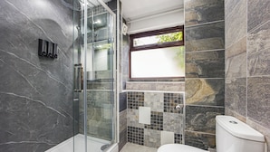 A bathroom with a glass shower enclosure, a toilet, and a window providing natural light. - Verv London Stratford (London)