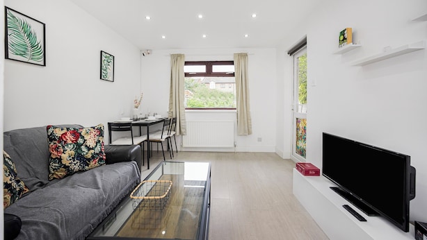 A modern living room with a sofa, a coffee table, a TV, and a dining area with a table and chairs. - Verv London Stratford (London)