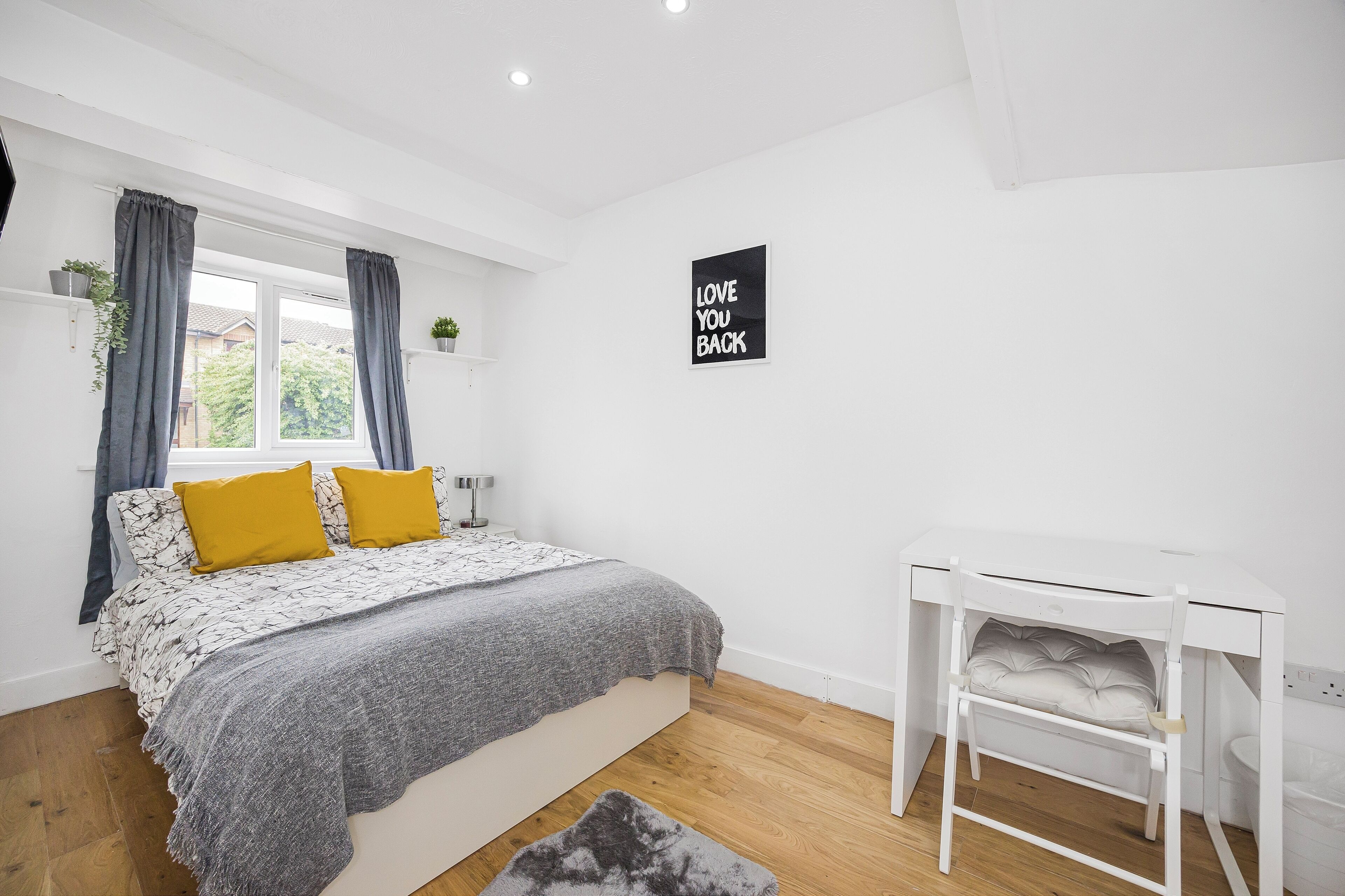 Ett sovrum med en säng, ett skrivbord och ett fönster med gardiner.