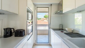 A narrow kitchen with white cabinets, a toaster, a kettle, and a small window overlooking a balcony.