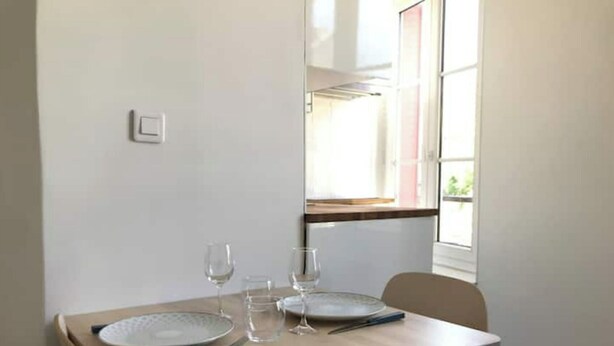 Una mesa de comedor con platos, vasos y cubiertos, una silla y una ventana con vistas a zonas verdes.