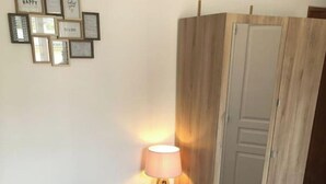 Un dormitorio con cama, almohadas, lámpara de noche, armario y cuadros en la pared.