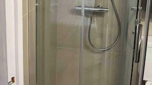 Ducha con cerramiento de vidrio, cabezal de ducha manual y grifo empotrado.