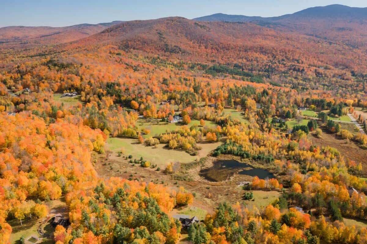 A rural landscape with autumn foliage, scattered houses, and rolling hills.