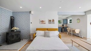 A modern bedroom with a bed, a fireplace, a dining area, and a kitchen in the background. - Renovated Condo in Luxury Neighborhood (Stowe)
