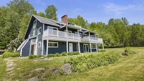 A two-story house with a balcony, surrounded by a well-maintained lawn and trees. - Renovated Condo in Luxury Neighborhood (Stowe)