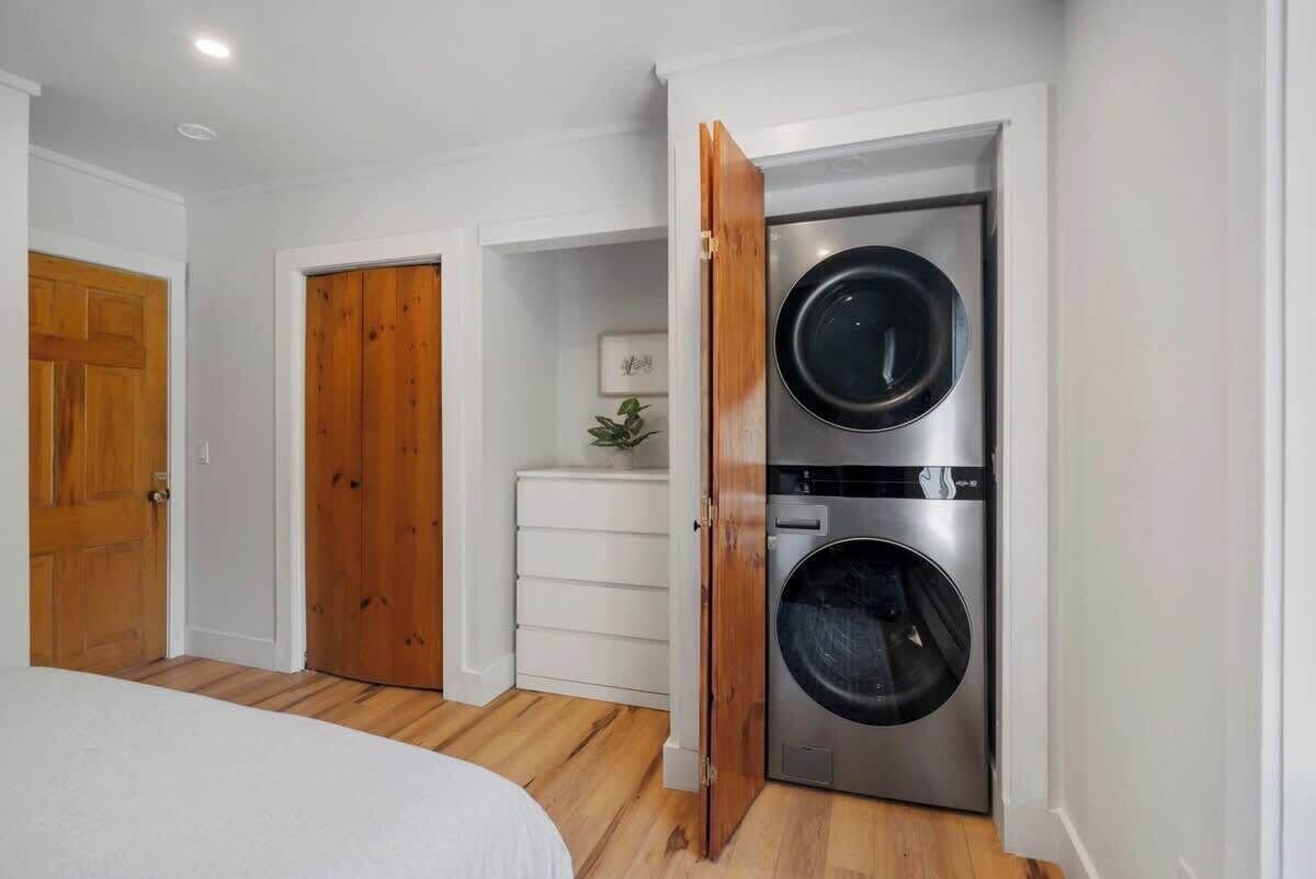 Ein Schlafzimmer mit Bett, Holztür, weißem Schminktisch und integriertem Edelstahl-Wasch- und Trockner.
