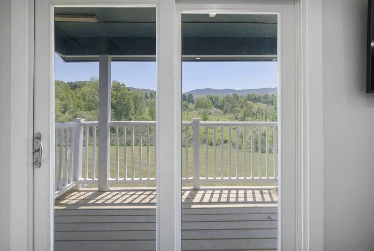 A view from a balcony with a white railing, overlooking a green landscape with trees and hills.