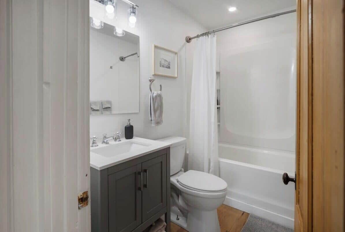 Ein modernes Badezimmer mit einem weißen Waschbecken, einem Waschtisch und einer Toilette, einer Dusche mit Glastür und einem gerahmten Bild an der Wand.