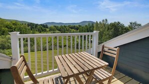 Una terraza de madera con una mesa y sillas, con vistas a un área verde con árboles y colinas al fondo.