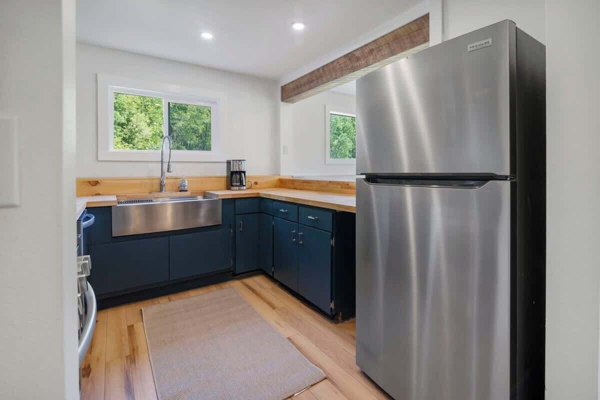A modern kitchen with a stainless steel refrigerator, dark blue cabinets, a wooden countertop, and a window with a view of greenery.