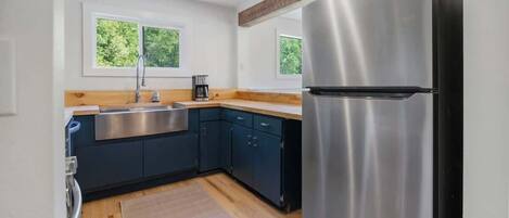 Una cocina moderna con un refrigerador de acero inoxidable, armarios azul oscuro, una encimera de madera y un ventanal con vistas al verdor.