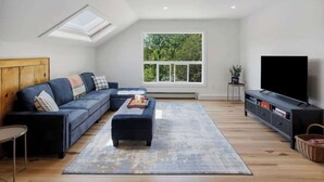 A modern living room with a sectional sofa, a flat-screen TV, and a skylight.