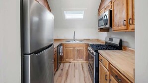A compact kitchen with wooden cabinets, a stainless steel refrigerator, a microwave, and a gas stove.