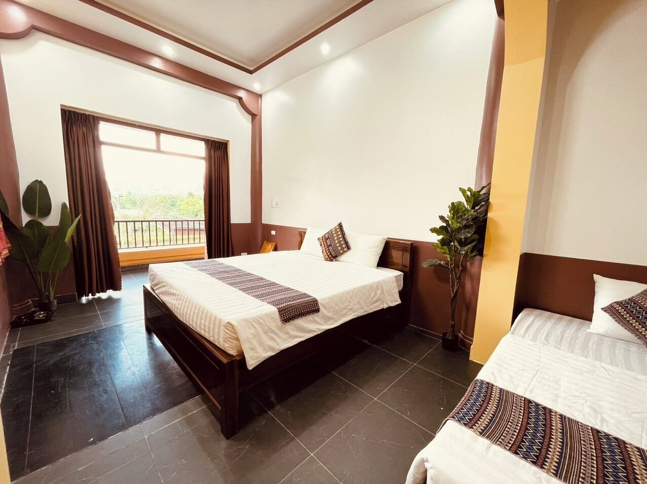 A hotel room with a large bed, a smaller bed, a balcony, and a potted plant.