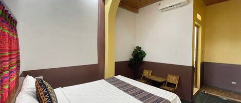 Ein Hotelzimmer mit einem Bett, einem Sessel, einem kleinen Tisch und einer Topfpflanze.