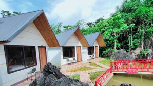 A resort with three cabins, each with a wooden roof and large windows, set against a backdrop of lush greenery and a rocky landscape. - Ha Giang Wings Bungalow (Ha Giang 1)