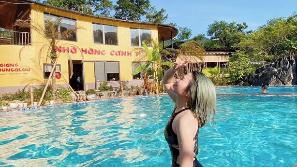 A swimming pool with a person in the water, a building with a sign, and surrounding greenery. - Ha Giang Wings Bungalow (Ha Giang 1)
