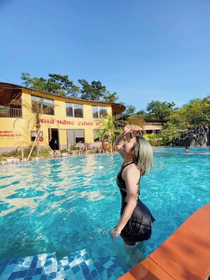 Una piscina con una persona nadando, un edificio con un letrero y follaje circundante.