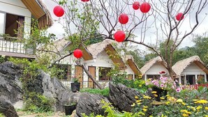 A traditional-style building with thatched roofs and a garden with large rocks and flowering plants. - Ha Giang Wings Bungalow (Ha Giang 1)