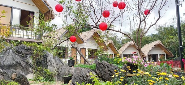 A traditional-style building with thatched roofs and a garden with large rocks and flowering plants.