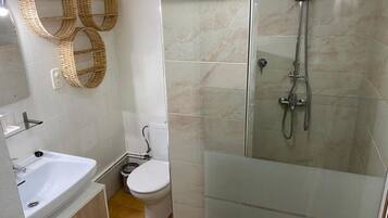 Un baño con ducha acristalada, un lavamanos blanco, un inodoro y dos adornos de mimbre en la pared.