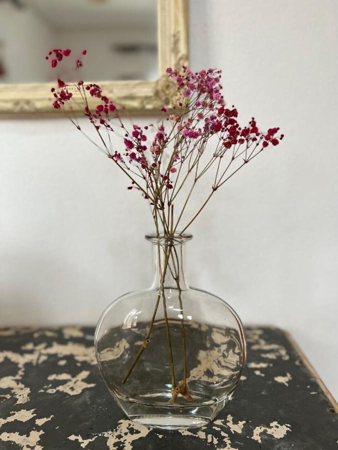 Un jarrón de vidrio transparente con flores rosadas sobre una mesa negra desgastada.
