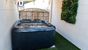 A hot tub in a narrow space with artificial grass, surrounded by white walls and a decorative metal fence. - L'étoile D'arras (Arras)