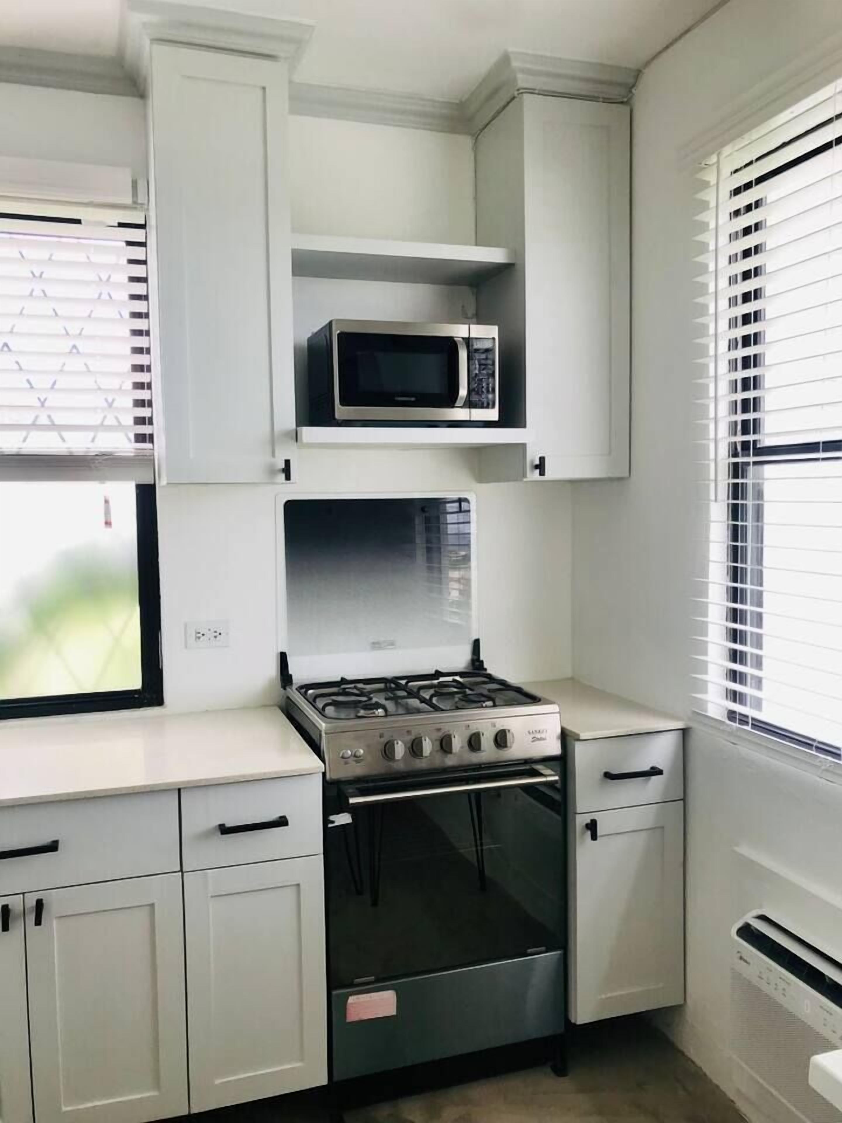 A compact kitchen with white cabinetry, a built-in microwave, a gas stove, and a small oven.