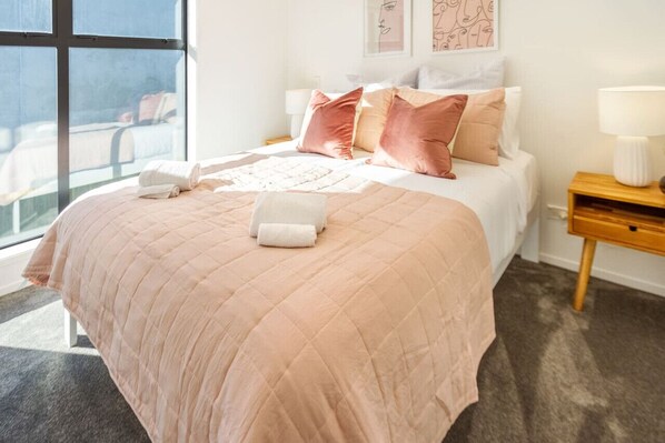 A neatly made bed with a pink quilt, two pillows, and a white throw blanket.