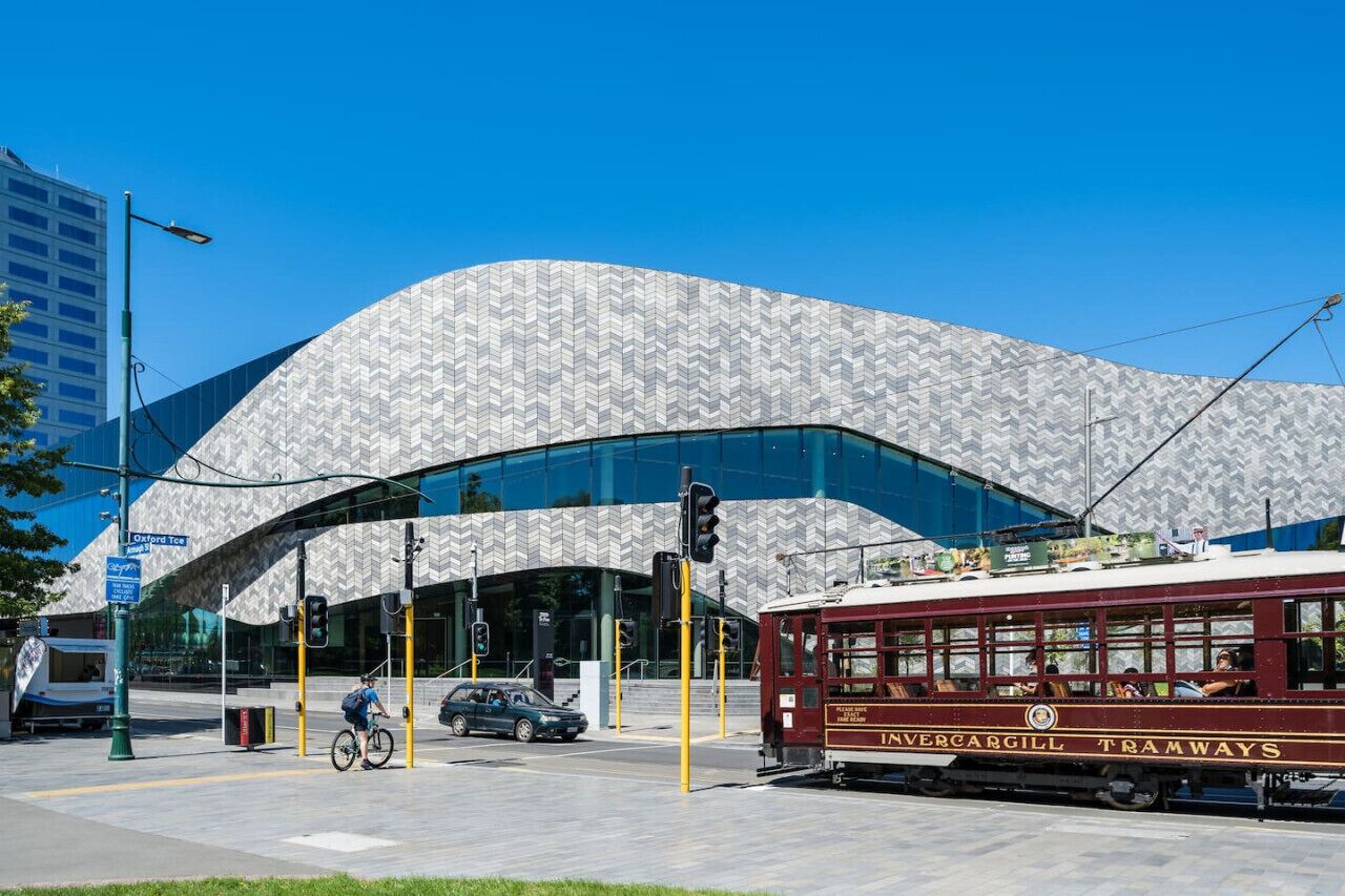 A tram at a tram stop with a modern building in the background.