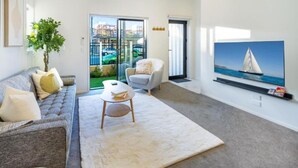 A living room with a sofa, armchair, and a coffee table. There is a large window with a view of a green space and a sailboat on the water. - Large trendy 3 Bedroom Residence, Central City (Christchurch)