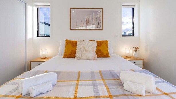 A hotel room with a large bed, two bedside tables, a window, and a wall-mounted picture. - Large trendy 3 Bedroom Residence, Central City (Christchurch)