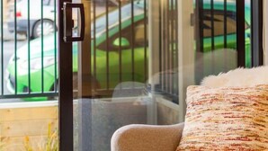A modern living room with a beige sofa, a glass door leading to a balcony, and a small table with a book and a remote control. - Large trendy 3 Bedroom Residence, Central City (Christchurch)