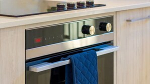 A modern kitchen with a built-in oven, a digital clock, and a blue towel hanging on the oven door. - Large trendy 3 Bedroom Residence, Central City (Christchurch)