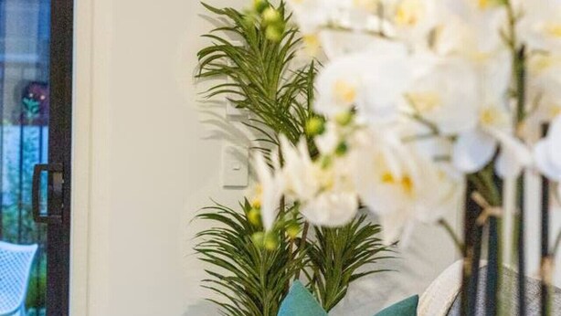Een eethoek met een tafel gedekt voor twee personen, een vaas met witte bloemen en uitzicht op een tuin door een glazen deur.