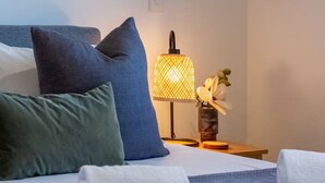 Een opgemaakt bed met kussens, een bedlampje en een vaas met bloemen.