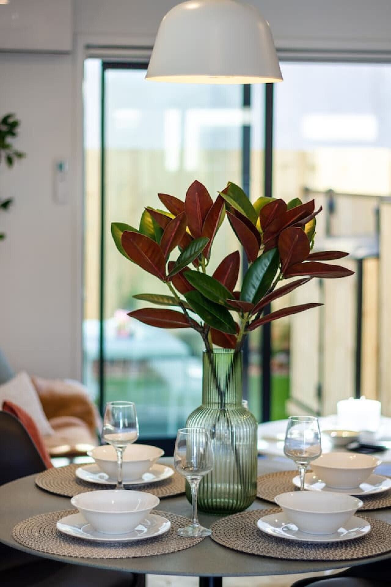 A dining table with a green vase, white plates, and wine glasses.