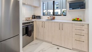 Een moderne keuken met lichte houten kastjes, een roestvrijstalen koelkast, een magnetron en een raam met uitzicht op de stad.