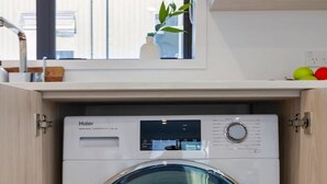 Een compacte, voorlader wasmachine van Haier in een houten kast, met een bedieningspaneel en een digitaal scherm.