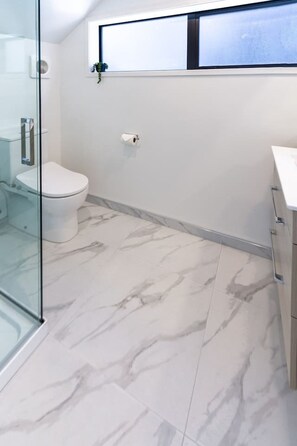 Een moderne badkamer met een toilet, een douchecabine van glas en een marmeren vloer.