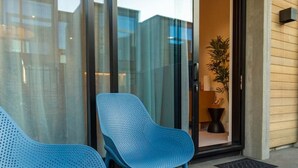 Un edificio moderno con puerta de cristal, dos sillas azules afuera y una planta en maceta adentro.