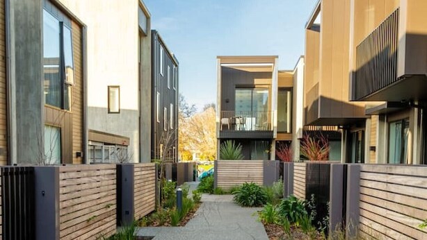 Un complejo residencial moderno con un sendero central flanqueado por edificios con amplias ventanas y balcones.