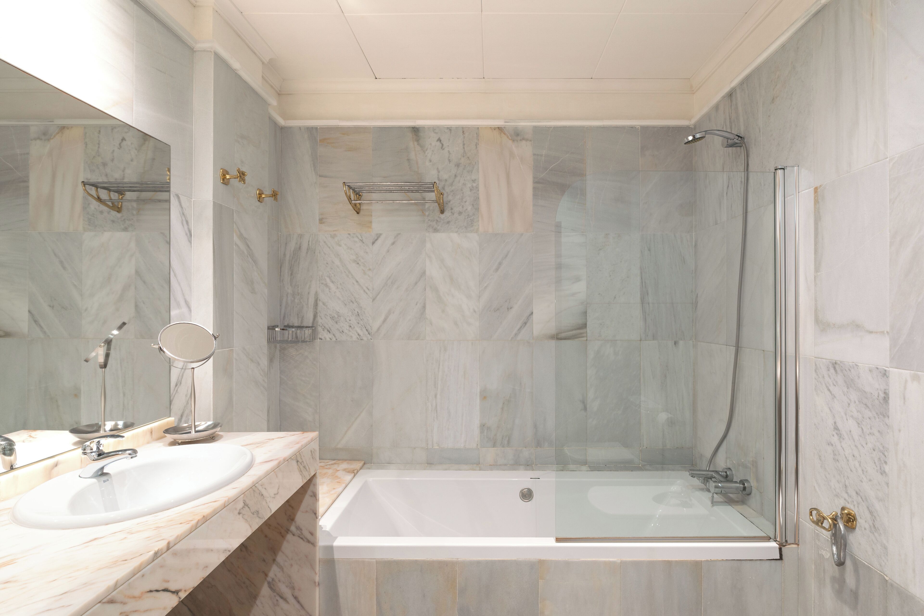 A modern bathroom with a marble sink, a glass-enclosed shower, and a large mirror.