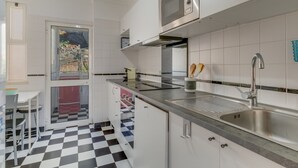 Moderni keittiö, jossa on valkoiset kaapit, ruostumattomasta teräksestä valmistettu pesuallas, mikroaaltouuni ja ruutukuviollinen lattia.