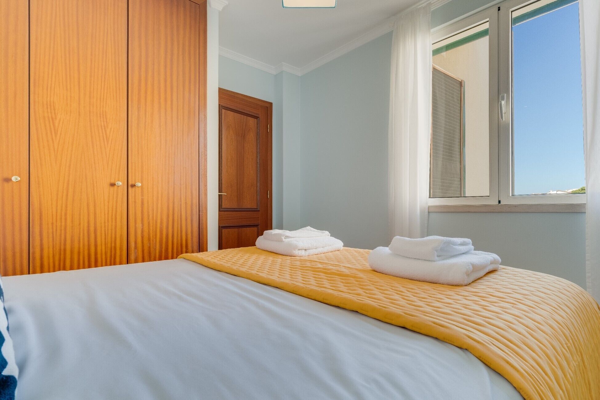 A bedroom with a bed, a wooden wardrobe, and a window with blinds.